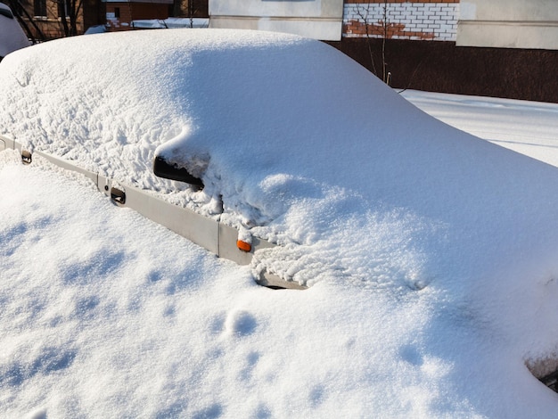 Automobile bianca sotto il cumulo di neve nel parcheggio