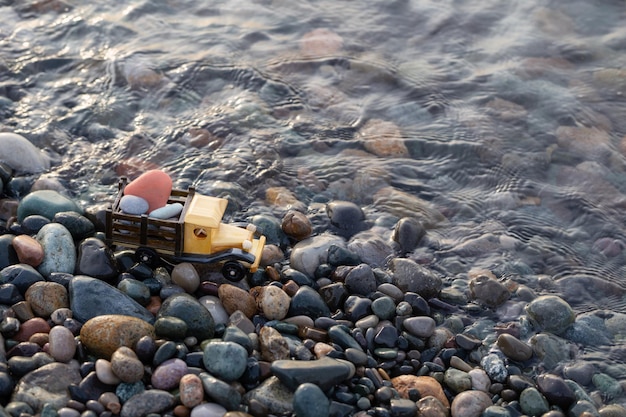 Automobile di legno del giocattolo sulla spiaggia del mare con le rocce al tramonto