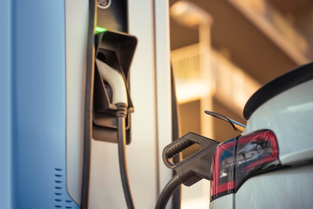 Automobile elettrica bianca che carica la batteria alla stazione di ricarica