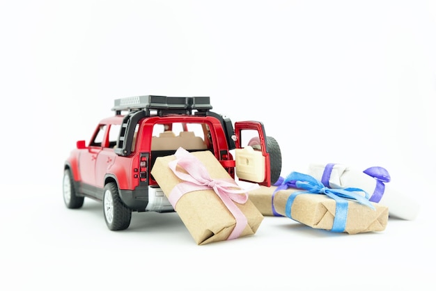 Automobile rossa del giocattolo che consegna il boxex del regalo presente sullo spazio bianco della copia del fondo