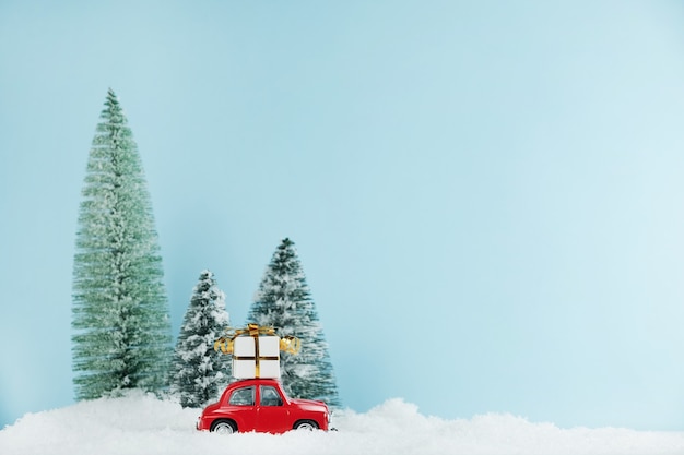 Automobile rossa di Natale con una confezione regalo in una pineta innevata. Carta di felice anno nuovo