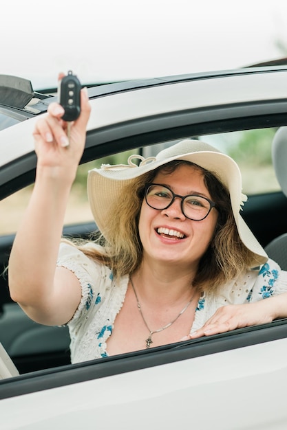 Automobilista donna sorridente che mostra le nuove chiavi della macchina e auto Femmina che guida cabrio in affitto durante le vacanze estive