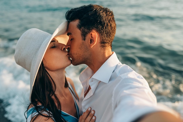 Autoritratto del primo piano della coppia innamorata che si bacia Luna di miele della giovane coppia felice Famiglia in vacanza Uomo bello e bella donna che fanno selfie sulla spiaggia e le onde del mare