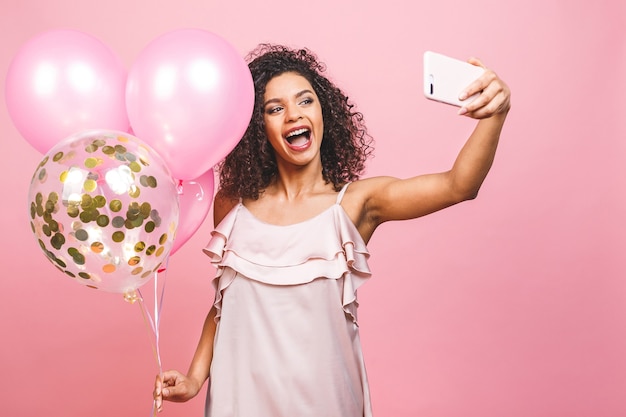 Autoritratto della ragazza afro americana positiva in vestito con palloncini in mano tiro selfie