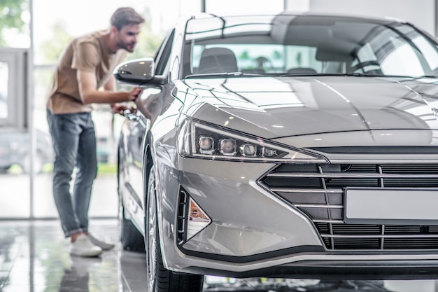 Autosalone. Cliente maschio esaminando auto nuove, piegandosi, guardando dentro