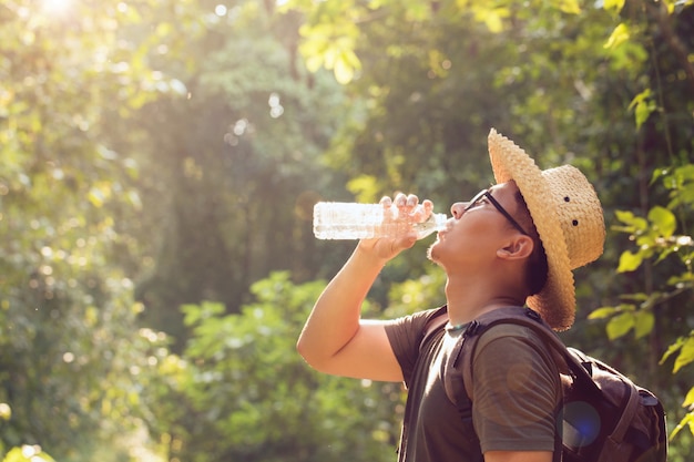 Autostoppista asiatico dell'uomo che prende una pausa per bere dalla bottiglia di acqua mentre facendo un'escursione al fondo della natura