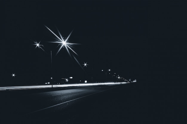 Autostrada nella città di notte con i lampioni stradali e le esposizioni di luce lunghe di esposizione dalla priorità bassa delle automobili