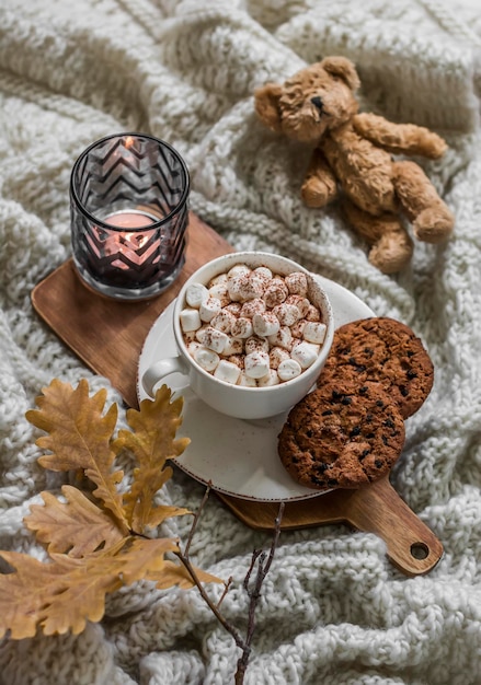 Autunno accogliente casa ancora vita cioccolata calda con marshmallow gocce di cioccolato biscotti foglie di quercia ramo orsacchiotto giocattolo candela su un'accogliente coperta a maglia vista dall'alto