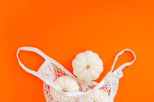 Autunno composizione piatta laici con zucche bianche in borsa della spesa in rete su sfondo di colore arancione audace.