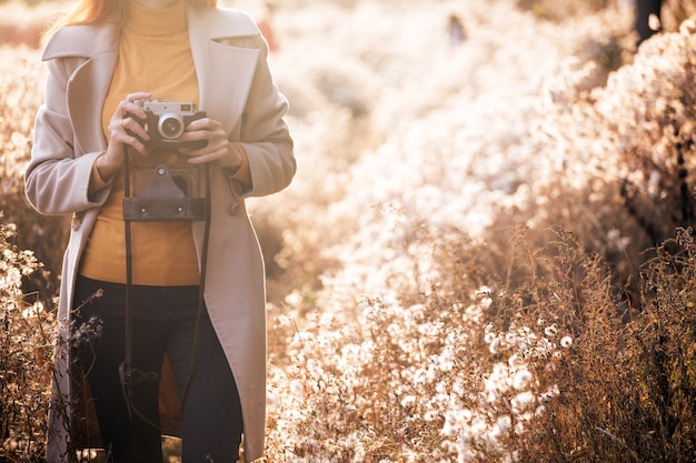 Autunno d'epoca. ragazza con una macchina fotografica vintage cammina nei campi di soffici denti di leone al tramonto