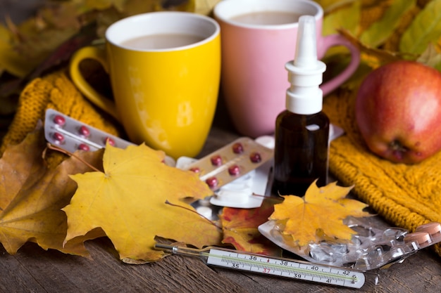 Autunno e sanità. tazza di tè, pillole e termometro su uno sfondo di legno