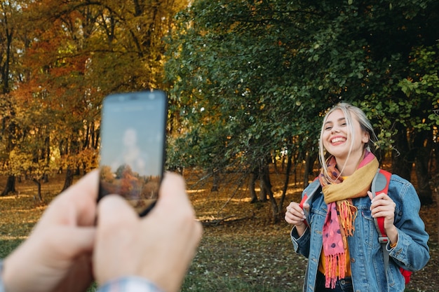 Autunno escursionismo uomo utilizzando la fotocamera dello smartphone per scattare una foto della sua ragazza nella foresta di autunno