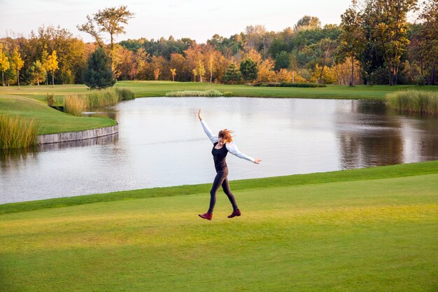 Autunno, lago, campo da golf. Giovane donna adulta in esecuzione sull'erba verde del campo da golf.