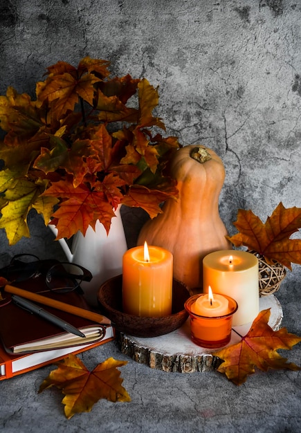 Autunno natura morta Candele accese bouquet di foglie d'acero libri zucca su sfondo grigio