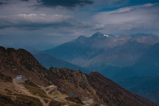 Autunno nel Caucaso settentrionale, località sciistica di Rosa Khutor in bassa stagione. Russia, Soci. Tonificazione vintage. Sfondo di viaggio. Paesaggio con la luce del sole che splende attraverso le nuvole e la nebbia arancioni.