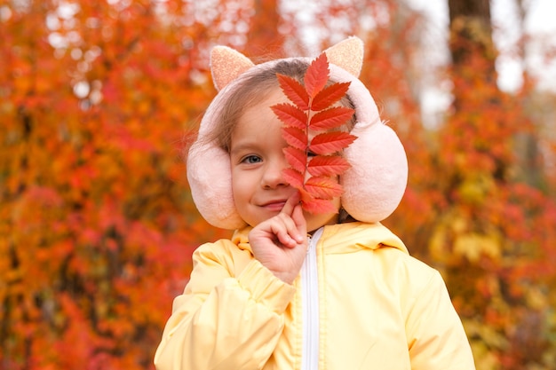 Autunno. Ritratto di una bambina carina che si nasconde dietro una foglia autunnale rossa. Camminare nel Parco. Foto di alta qualità