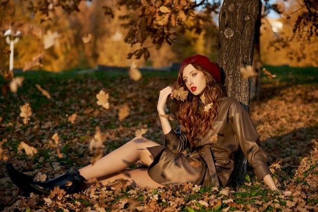 Autunno ritratto di una donna in un cappello berretto e impermeabile vicino a un albero in autunno fogliame giallo