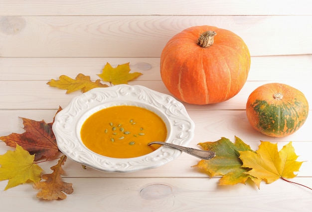 Autunno still life di zuppa di zucca, foglie di acero e quercia, zucca intera