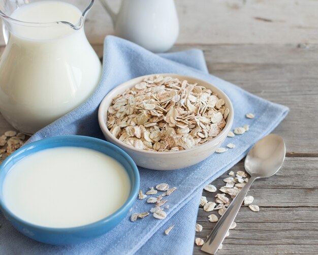 Avena rotolata in una ciotola e latte su una fine del tavolo di legno su