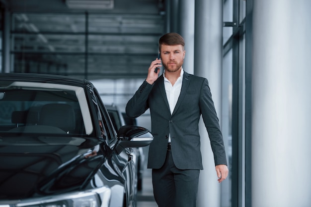 Avere conversazione. Moderno ed elegante uomo d'affari barbuto nel salone dell'automobile.