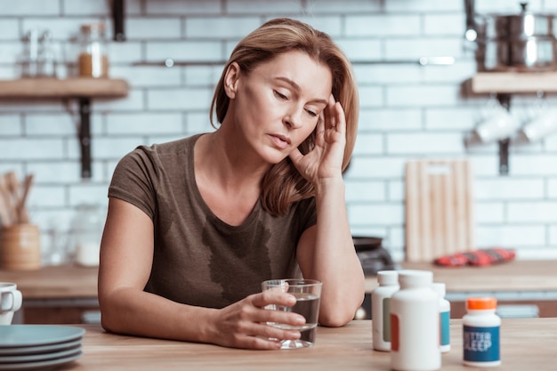 Avere mal di cuore. Donna depressa e stressata dai capelli biondi che ha mal di cuore che versa acqua sulla maglietta