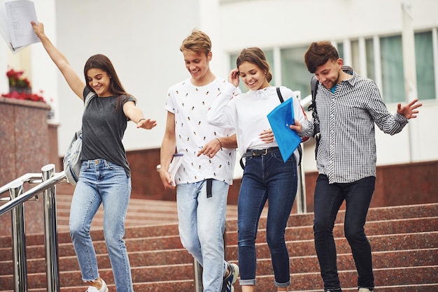 Avere un buon umore e una buona conversazione. Gruppo di giovani studenti in abiti casual vicino all'università durante il giorno.