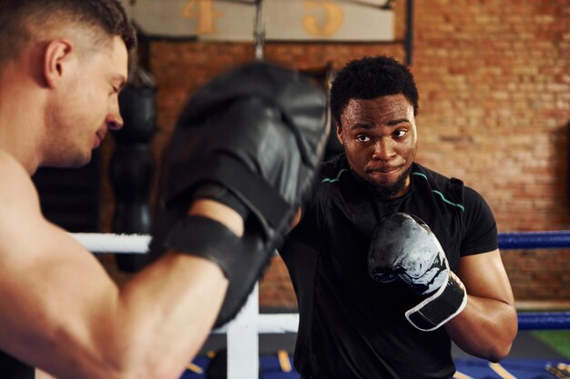 Avere una pratica di boxe afroamericano con un ragazzo bianco ha una giornata di allenamento in palestra