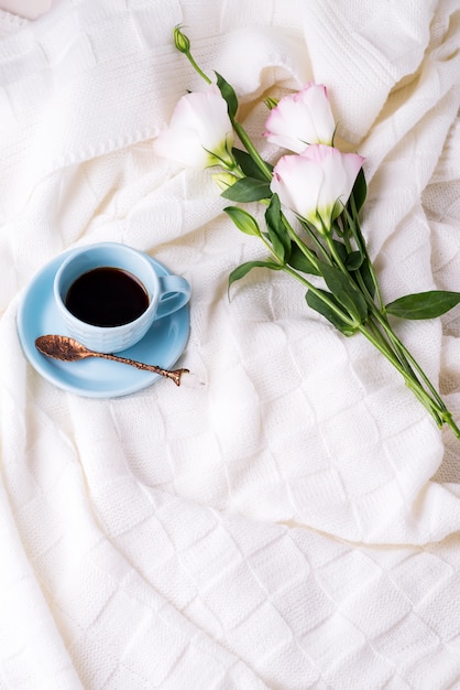 Avere una tazza di caffè con cioccolato, fiori eustoma sulla coperta nel letto.