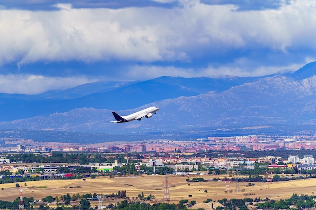 Avio generico che decolla e prende quota accanto a una città e grandi montagne sullo sfondo