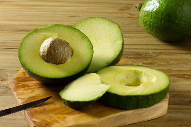 Avocado affettato a coltello su base di legno su tavola rustica con avocado sullo sfondo