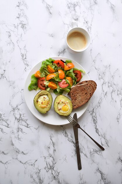 Avocado al forno con uova di quaglia Salat al pomodoro e tazza di cappuccino