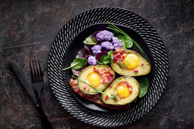 Avocado al forno con uovo e pancetta, piatto giaceva sul muro scuro