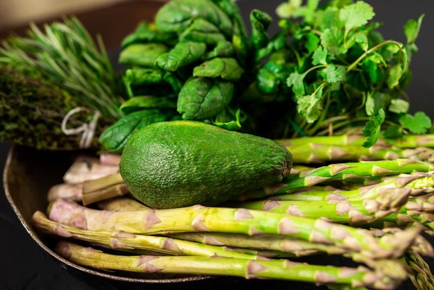 Avocado e varie verdure verdi su sfondo scuro Asparagi spinaci rosmarino Concetto di cibo vegetariano