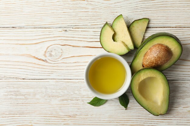 Avocado ed olio freschi maturi sulla tavola di legno bianca, vista superiore