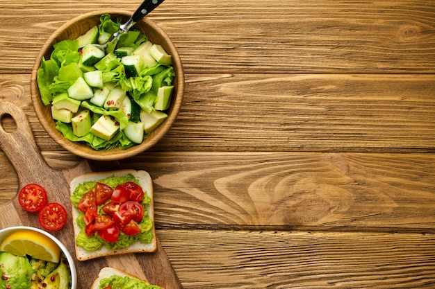 Avocado fracassato e toast di pomodori tritati, sana insalata di avocado verde sul tagliere su fondo marrone rustico in legno. Cibo vegetariano, spuntino sano per la dieta, mangiare pulito. Vista dall'alto, copia spazio