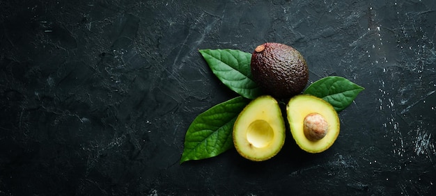 Avocado fresco con foglie su sfondo nero Vista dall'alto Spazio libero per il testo