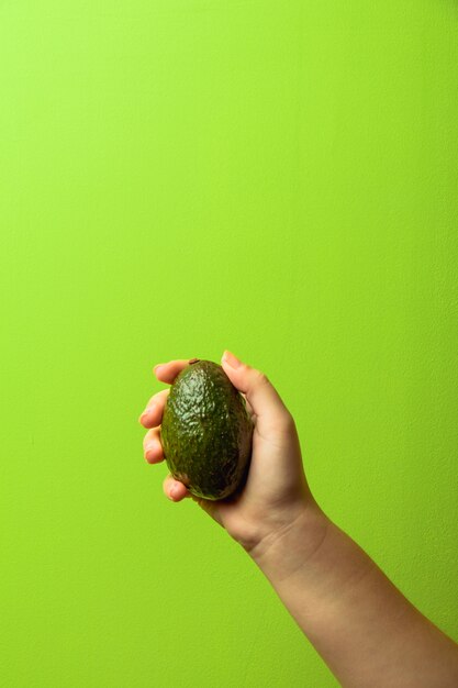 Avocado in una mano di sfondo verde donna. concetto di cibo sano