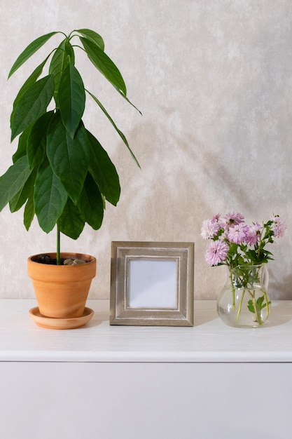 Avocado in vaso, cornice per foto, bouquet in vaso sul comò bianco