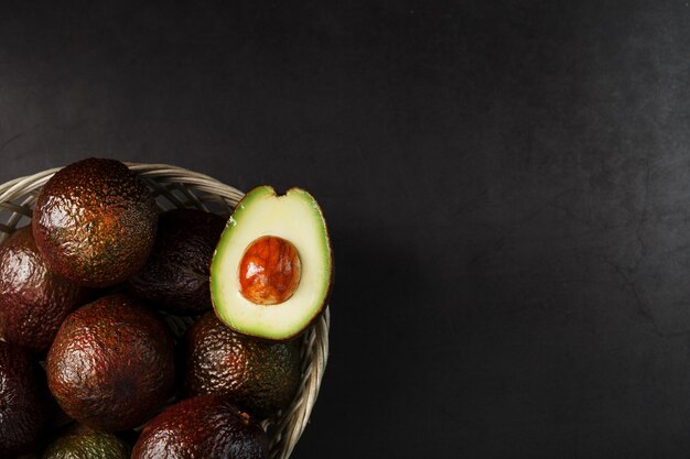 Avocado maturi in un cesto su una tavola nera, con un frutto tagliato e una pietra