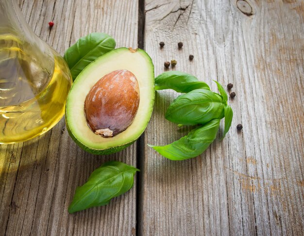 Avocado, olio e basilico su fondo di legno vecchio.