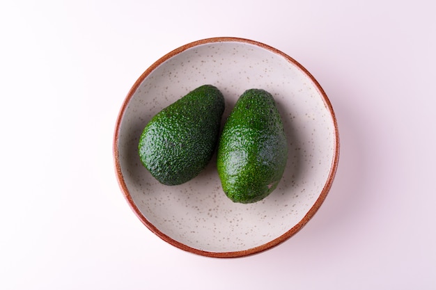 Avocado succosi maturi in un piatto ceramico fatto a mano isolato