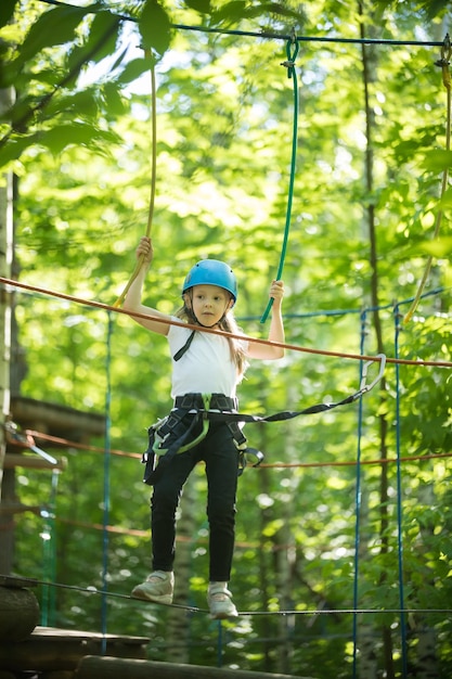 Avventura di corda nella foresta una bambina in piedi sul ponte di corda con l'assicurazione completa