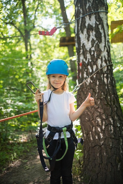 Avventura estrema con la corda una bambina con una cintura assicurativa in piedi nel parco e con in mano un gancio assicurativo