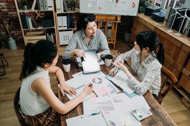 avviare riunioni di lavoro in un ambiente di lavoro moderno. Vista dall'alto dei partner del team femminile che fanno brainstorming con la tavoletta digitale mentre sono seduti insieme in ufficio. tre colleghe che discutono di un nuovo progetto.