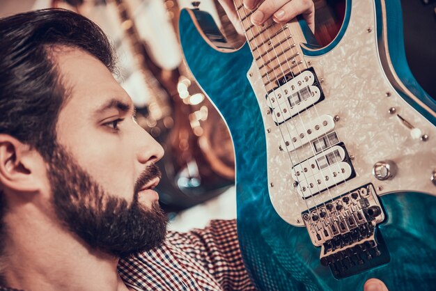 Avvicinamento. L&#39;uomo barbuto adulto esamina strettamente la chitarra elettrica