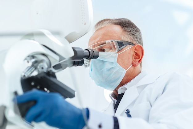 Avvicinamento. scienziato in una maschera protettiva guardando attraverso un microscopio. scienza e tutela della salute.