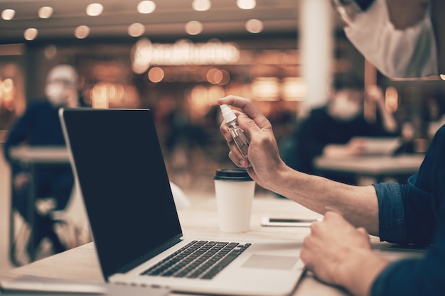 Avvicinamento . visitatore del caffè che spruzza antisettico sul suo laptop. foto con copia-spazio