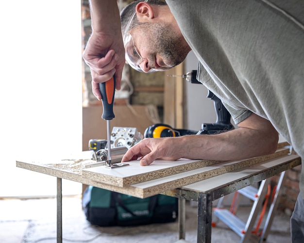 Avvitare una vite autofilettante in un foro di fissaggio metallico su un listello di legno usando un cacciavite, opera di un falegname.