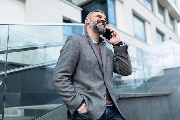 Avvocato maschio adulto sorridente maturo con barba e capelli grigi parla al telefono