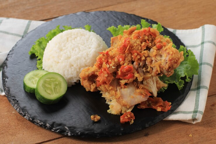 Ayam Geprek è il cibo di strada popolare in Indonesia. Fatto da pollo croccante schiacciato in Sambal Bawang (salsa di peperoncino e aglio). Servito con Riso e Verdure